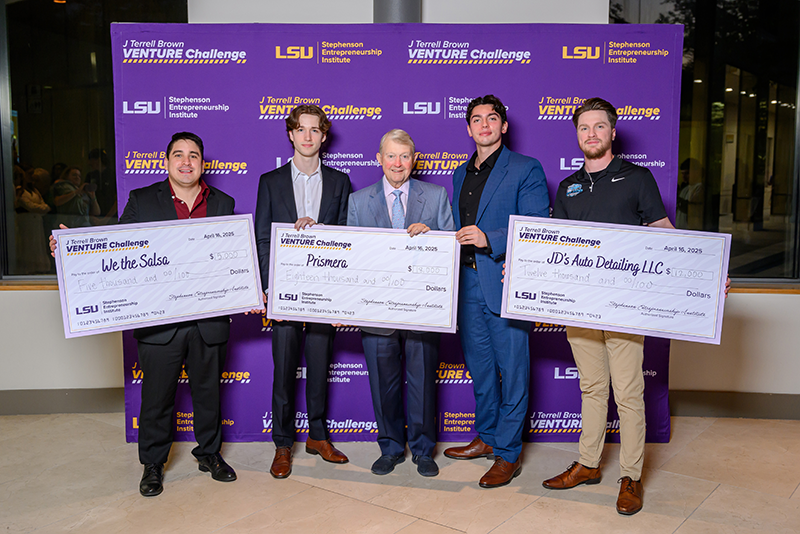 Students hold giant cardboard checks and smile with excitement as prizes are distributed on stage at the 2024 J Terrell Brown Venture Challenge.