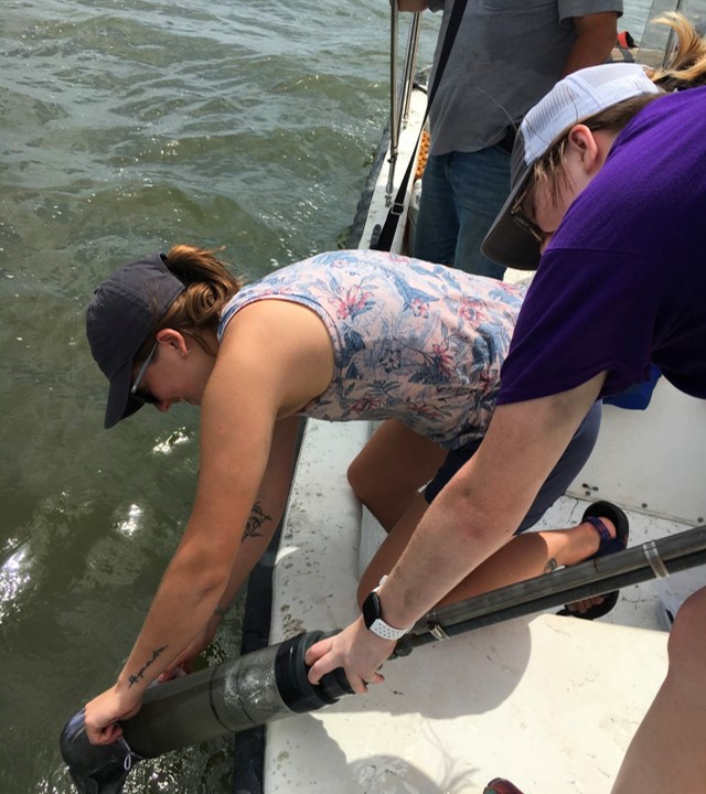 Core Sampling Researchers reach over the side of a boat to retreive a core sample